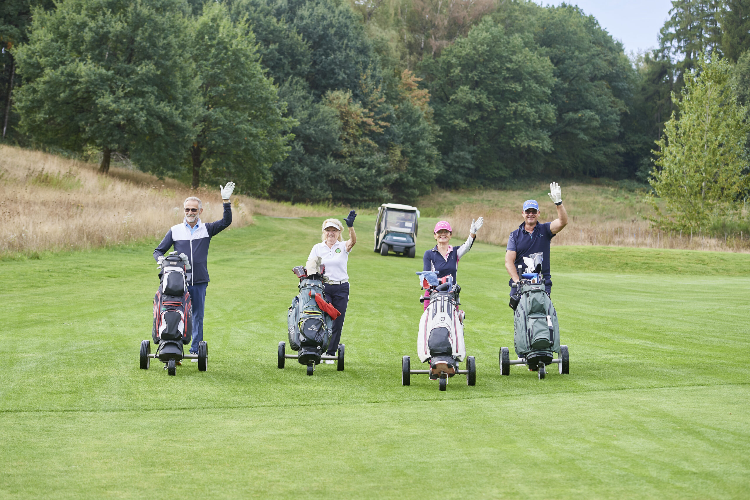 Vier gut gelaunte Golferinnen und Golfer winken mit ihren Trolleys auf dem Fairway des GC Weiherhof beim 27. Charity Golf-Cup Play for Life